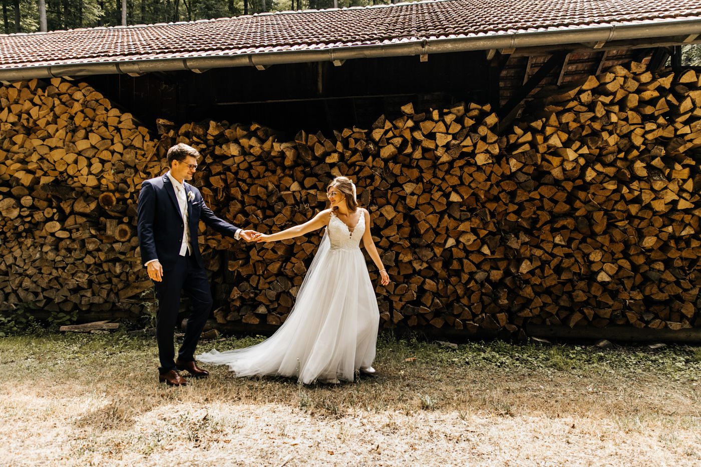 Hochzeitsfotograf fängt romantisches Brautpaar beim Fotoshooting auf dem Bauernhof ein – Hand in Hand am rustikalen Holzunterstand. Hochzeitsfotograf | Hochzeitsvideograf NRW