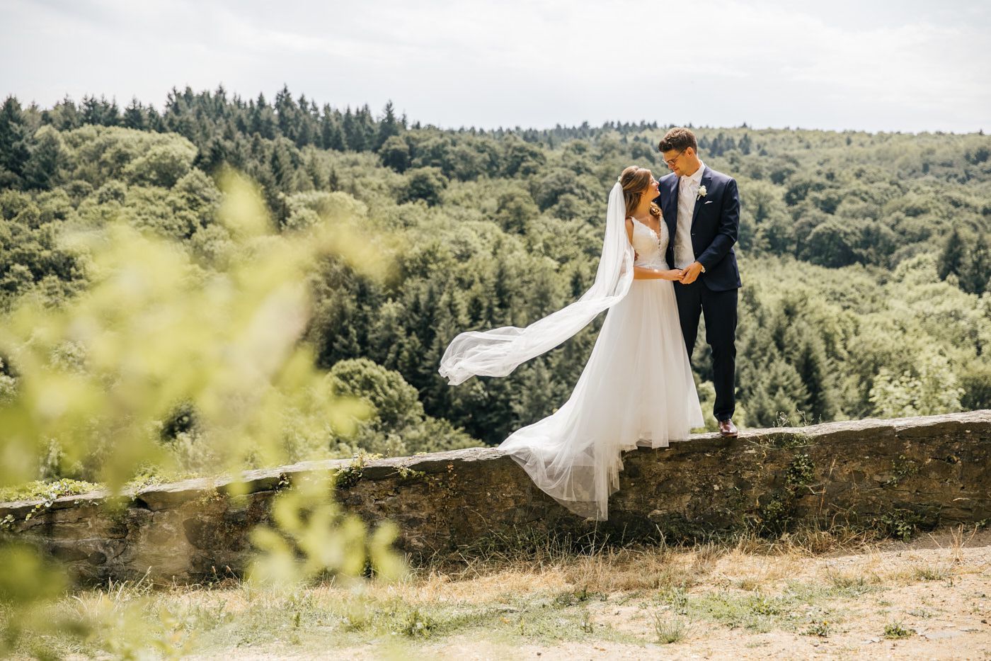 Brautpaar auf Steinmauer mit wehendem Schleier – Hochzeitsfotograf Detmold